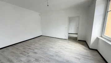 Helles, leeres Zimmer mit modernem Laminatboden und weißen Wänden, bereit für die individuelle Gestaltung.