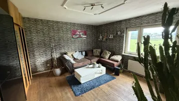 Gemütliches Wohnzimmer mit Holzboden, Steintapete und einem großen Fenster mit Blick ins Grüne.
