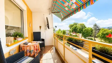 Heller Balkon mit bunter Markise, Sitzgelegenheiten und weitem Blick ins Grüne.