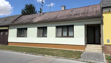Vorderansicht eines Einfamilienhauses mit braunen Fenstern und Rollläden unter blauem Himmel.