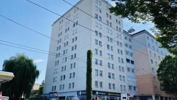 Mehrstöckiges Wohngebäude mit Geschäften im Erdgeschoss und parkenden Autos auf der Straße.