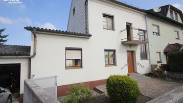 Vorderansicht des Hauses mit kleiner Gartenfläche, Balkon und Garagenzufahrt.