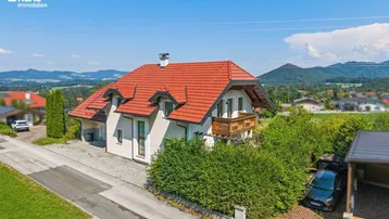 Freistehendes Einfamilienhaus mit rotem Ziegeldach, kleinem Balkon und Bergblick in ländlicher Umgebung.