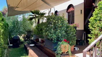 Große Holzterrasse mit Sonnensegel, vielen Pflanzen und gemütlicher Sitzecke im Freien.