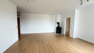 Helles Wohnzimmer mit hellem Laminatboden und einem modernen Holzofen in der Ecke.