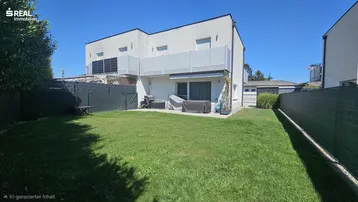 Hinterer Gartenbereich eines modernen Reihenhauses mit Rasenfläche und kleiner Terrasse.