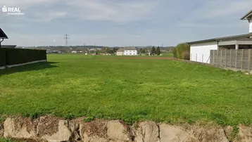 Grünes Baugrundstück mit weitem Blick auf die Landschaft und umliegende Häuser.