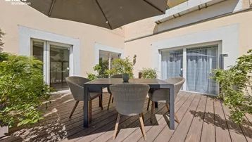 Große Holzterrasse mit Esstisch, Stühlen und Sonnenschirm, ideal für Mahlzeiten im Freien.