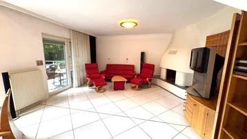 Gemütliches Wohnzimmer mit Kamin, Fliesenboden und Zugang zur Terrasse.
