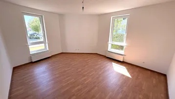 Helles Zimmer mit Holzfußboden und zwei Fenstern, die viel Tageslicht hereinlassen.