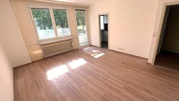 Helles Zimmer mit Laminatboden, großen Fenstern und Zugang zu einem Balkon.