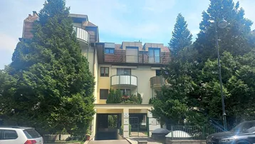 Mehrstöckiges Wohngebäude mit Balkonen und begrüntem Eingangsbereich unter blauem Himmel.