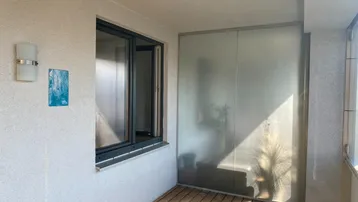 Heller Balkon mit Holzfußboden und Milchglas-Trennelement, ideal für entspannte Stunden im Freien.