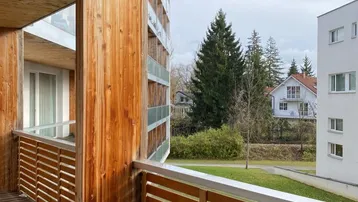Geräumiger Holzbalkon mit Blick ins Grüne und auf die umliegenden Gebäude, sehr naturnah.