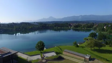 Weitläufiger Blick auf den klaren See, die majestätischen Berge und die grüne Landschaft unter blauem Himmel.