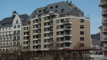 Mehrstöckiges Wohngebäude mit beiger Fassade, zahlreichen Balkonen und einem markanten Mansarddach in städtischer Umgebung.