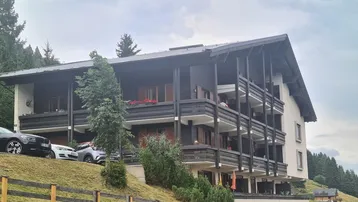 Mehrstöckiges Gebäude im alpinen Stil mit vielen Balkonen und umgeben von Bäumen.