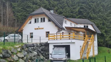 Weißes Einfamilienhaus mit Satteldach und integrierter Garage, umgeben von Wald.