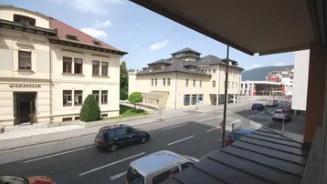 Blick von einem Balkon auf eine städtische Straße mit vorbeifahrenden Autos und umliegenden Gebäuden.
