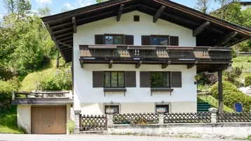 Traditionelles Alpenhaus mit weißer Fassade, Holzbalkonen und integrierter Garage in grüner Umgebung.