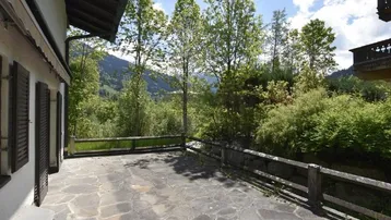 Geräumige Steinterrasse mit Holzzaun und weitem Blick auf die grüne Berglandschaft.