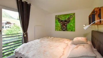 Schlafzimmer mit Doppelbett und Balkonzugang, bietet einen schönen Blick auf die umliegende Berglandschaft.