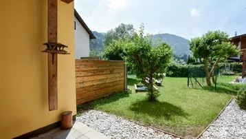 Kleiner Gartenbereich mit Rasenfläche, Bäumen und Kiesweg, umgeben von einer Berglandschaft.