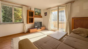 Helles Wohnzimmer mit beigem Sofa, Holzboden und Zugang zu einem Balkon, der viel Sonnenlicht hereinlässt.