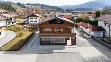 Traditionelles Holzhaus mit Satteldach und Geschäft im Erdgeschoss, umgeben von einer ländlichen Berglandschaft.