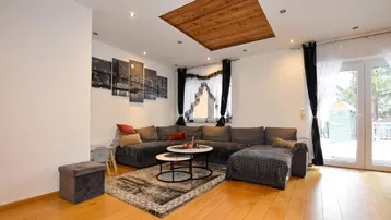 Helles Wohnzimmer mit großem Ecksofa, Holzboden und Zugang zu einem Außenbereich.