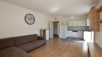 Heller offener Wohnbereich mit braunem Sofa, Holzboden und integrierter weißer Küchenzeile.