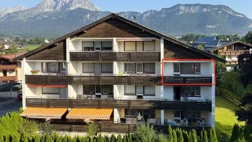Mehrfamilienhaus mit mehreren Balkonen und beeindruckendem Bergblick im Hintergrund.
