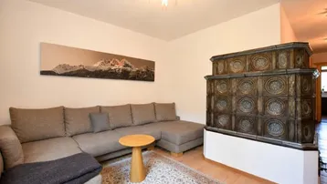 Gemütliches Wohnzimmer mit großem Sofa, traditionellem Kachelofen und Holzboden, ideal zum Entspannen.
