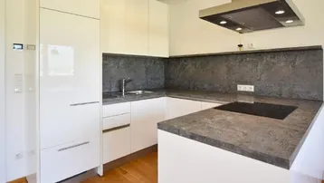 Moderne weiße Küche mit Hochglanzfronten, dunkler Arbeitsplatte und integriertem Induktionskochfeld.