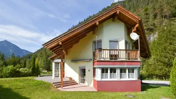Charmantes Chalet mit Holzbalkonen und Satteldach, umgeben von grüner Natur und Bergen.