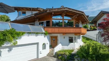 Charmantes Haus im alpinen Stil mit Garage, Holzelementen und Solaranlage unter blauem Himmel.