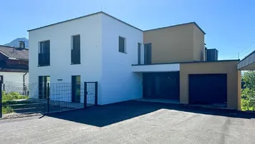 Moderne Architektur eines Neubaus mit weißer und beiger Fassade sowie integrierter Garage und Bergblick.