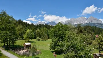 Weitläufige Grünfläche mit Spielplatz und beeindruckendem Bergblick unter blauem Himmel.