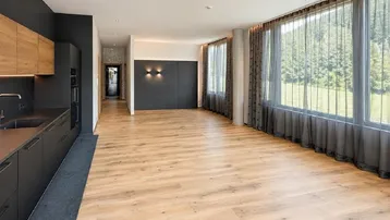 Geräumiger, offener Wohnbereich mit Holzboden, großen Fenstern und Blick ins Grüne.