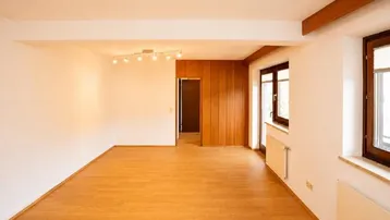 Heller, leerer Raum mit Holzboden, weißen Wänden und sichtbaren Holzbalken.
