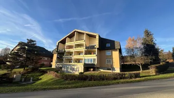 Modernes Mehrfamilienhaus mit gelber Fassade und mehreren Balkonen unter blauem Himmel.