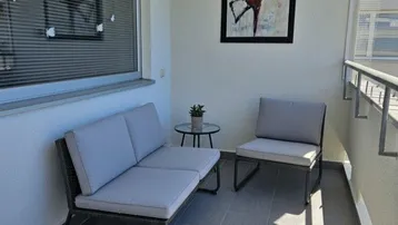 Heller Balkon mit modernen Outdoor-Möbeln und Fliesenboden, ideal zum Entspannen im Freien.