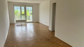 Helles Wohnzimmer mit Parkettboden, weißen Wänden und Zugang zu einem Balkon mit Bergblick.