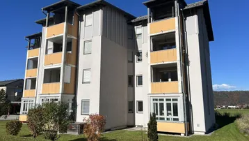Modernes Mehrfamilienhaus mit mehreren Balkonen und Loggien in einer grünen Umgebung.