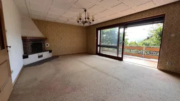 Geräumiges Wohnzimmer mit Kamin, Teppichboden und Zugang zum Balkon.