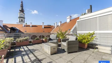 Geräumige Dachterrasse mit Sitzgelegenheiten und Blick auf die historische Kirchturmspitze.
