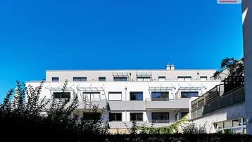 Moderne Wohnanlage mit weißer Fassade und blauen Akzenten unter klarem Himmel.