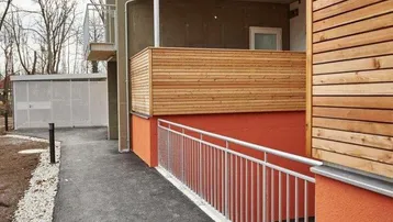 Moderner Eingangsbereich eines Neubaus mit barrierefreier Rampe und Holzverkleidung an den Balkonen.