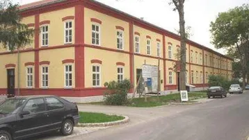 Gelbes Wohngebäude mit roten Fensterrahmen und traditioneller Architektur an einer ruhigen Straße.