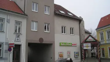 Gebäudeansicht mit gemischter Nutzung, inklusive eines Nahversorgers im Erdgeschoss und Wohnungen darüber.